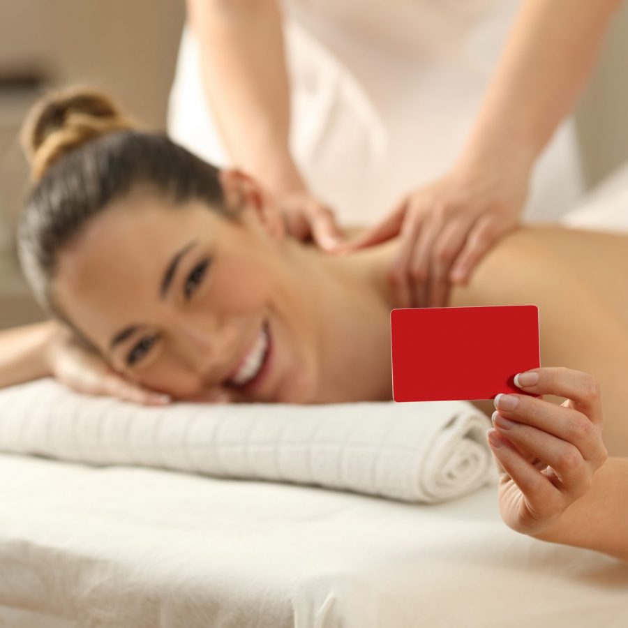 Happy woman receiving a massage showing blank credit or gift card in a spa salon